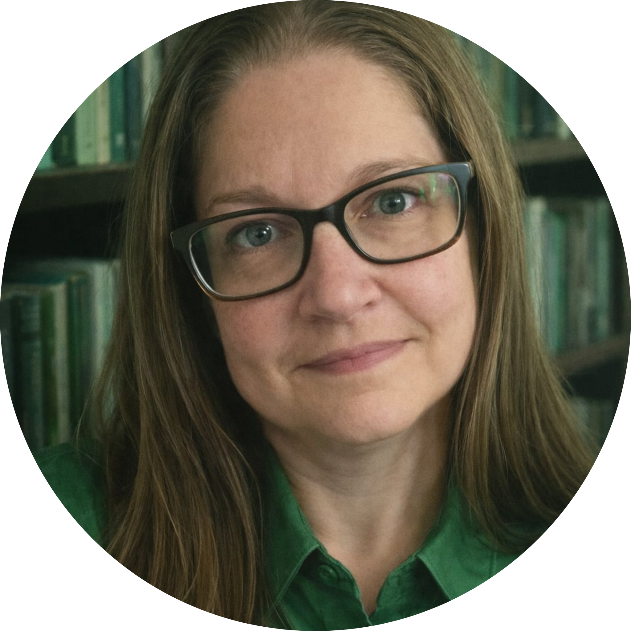 Portrait d’une femme portant des lunettes et une chemise verte, regardant la caméra devant une bibliothèque